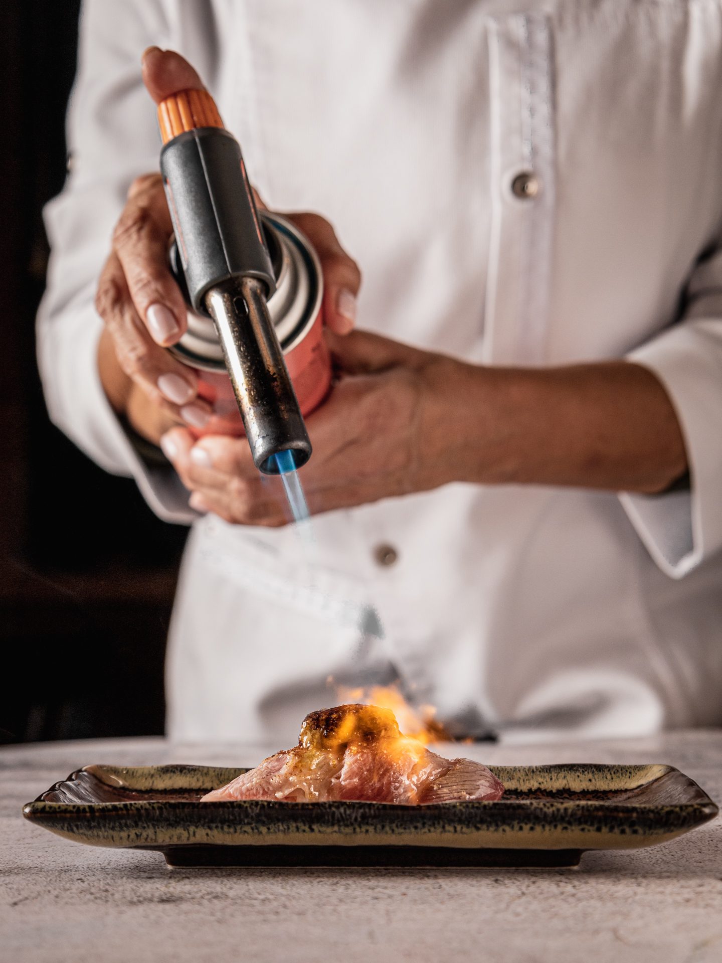 Chef torching nigiri on a ceramic plate